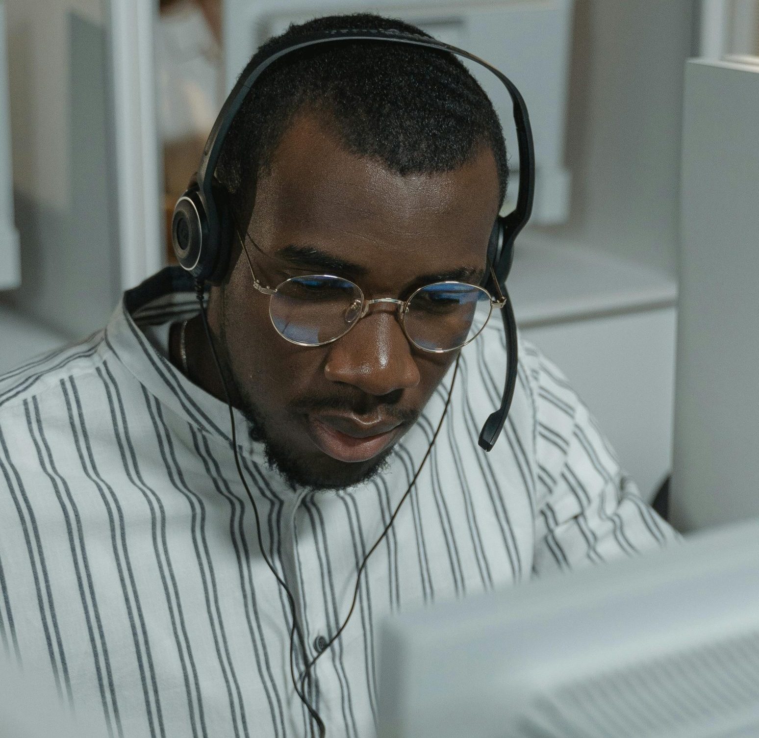 Customer support representative wearing glasses and headset in a busy call center setting.
