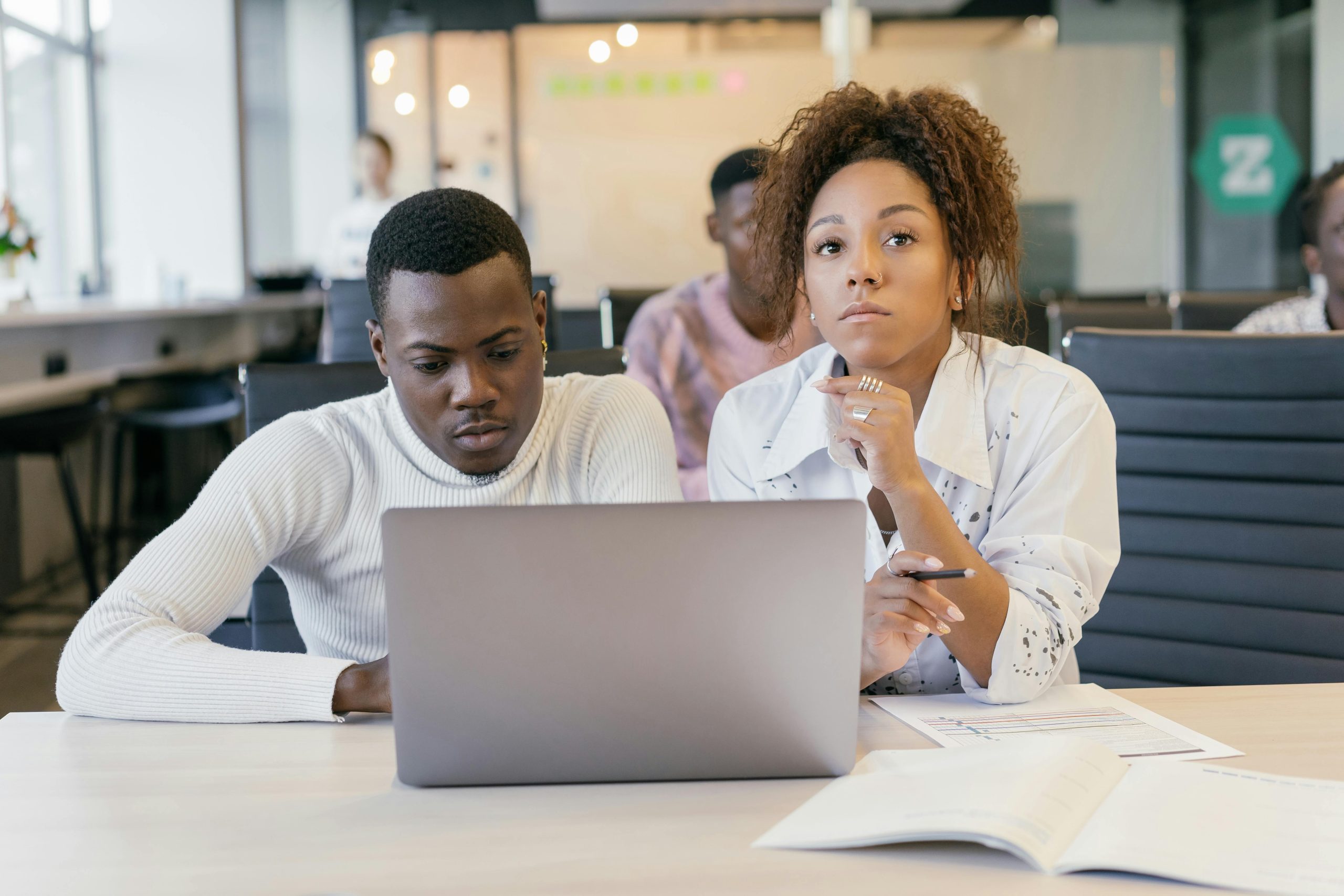 Two young professionals focused on a laptop in a modern office setting, collaborating on a project.